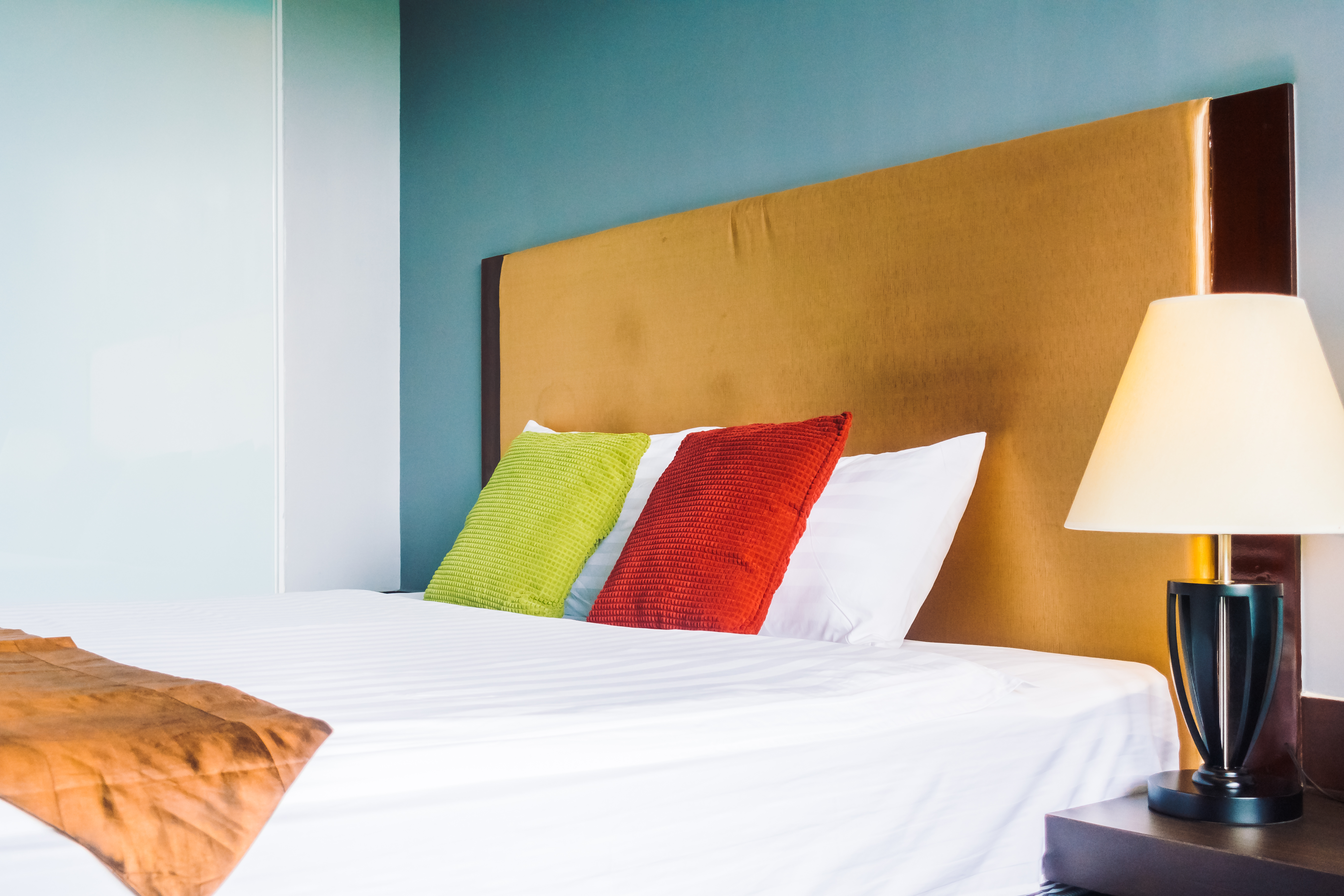 A simple bed adorned with a white sheet, accompanied by a lamp that provides soft illumination in the room.