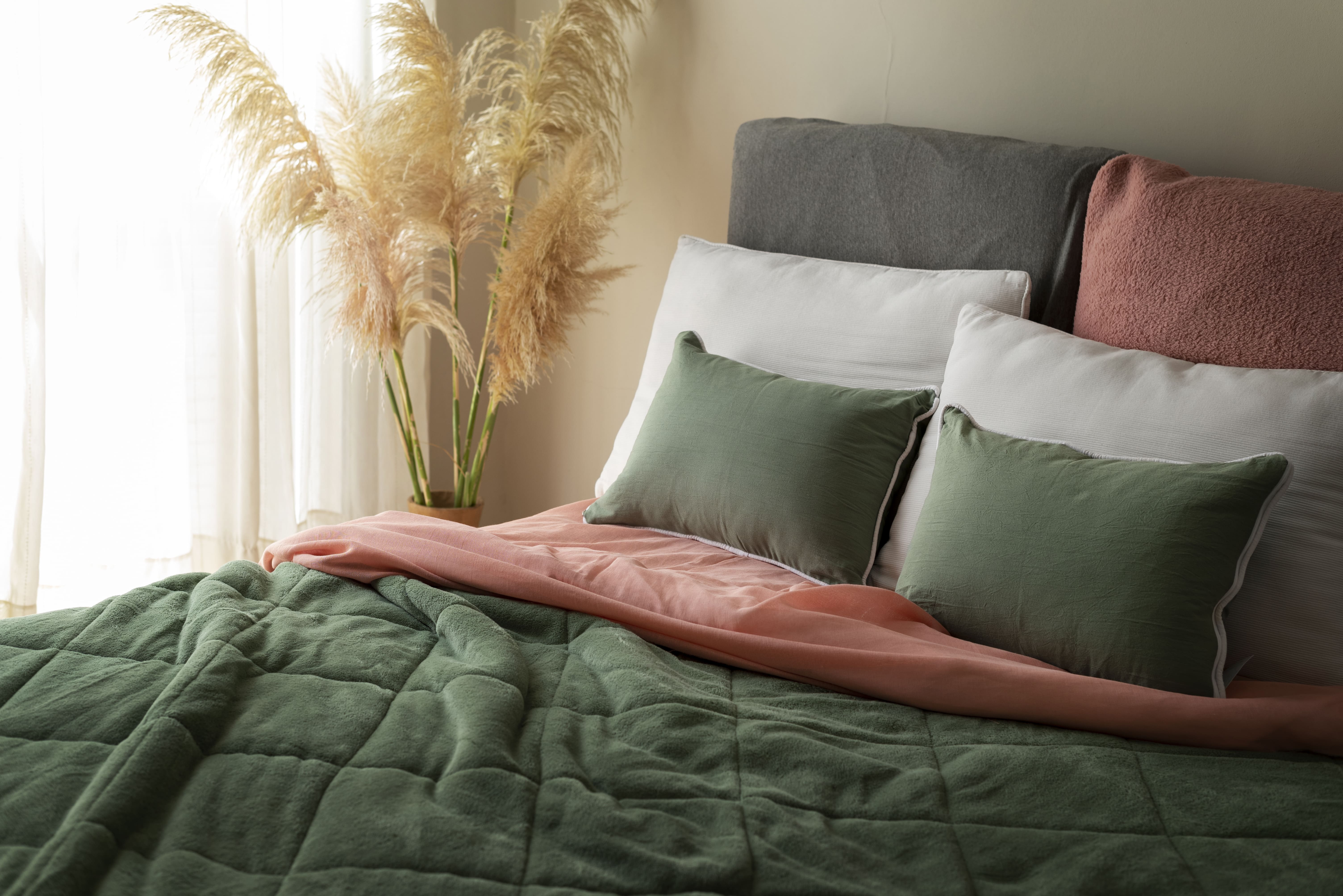 A beautifully arranged bed with vibrant green and pink pillows, alongside a vase of tall grass, enhancing the room's decor.