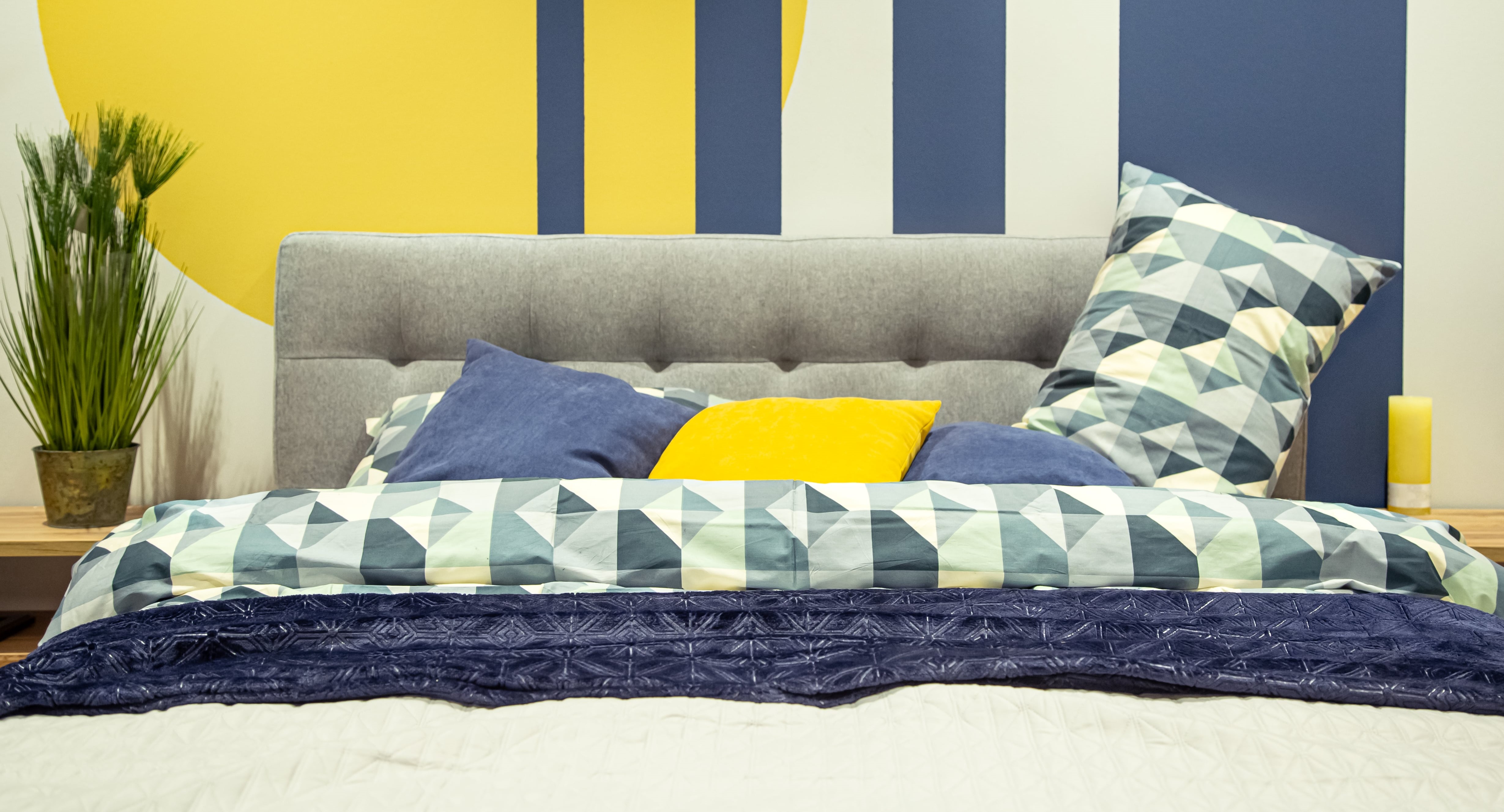 A stylish bed located in front of a blue and yellow striped wall, contributing to a bright and lively interior design.